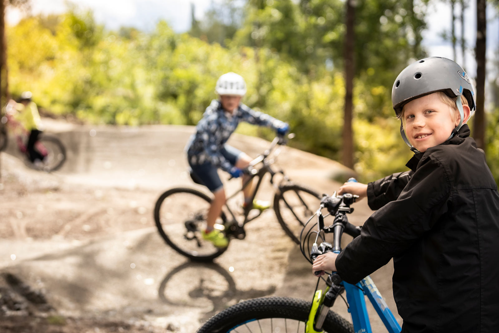 Barn och unga cyklar över grushinder i skogen. 