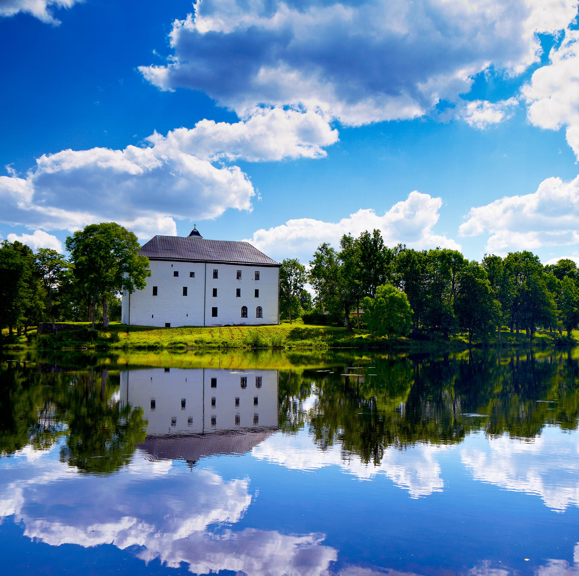 Vitt slott i grön omgivning med en sjö framför