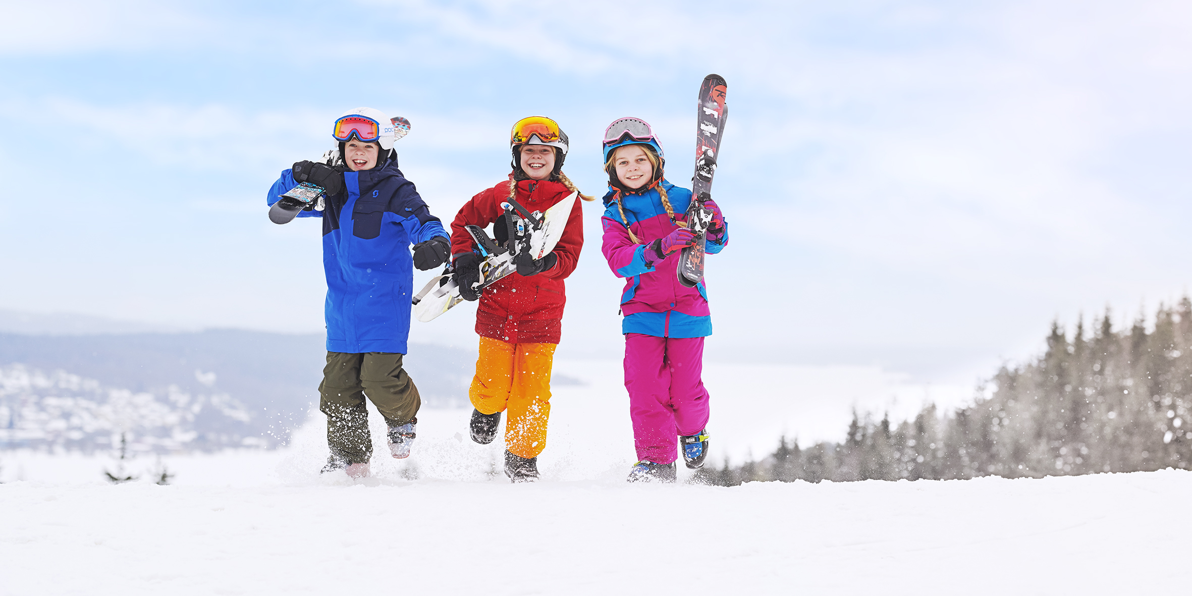Barn i färgglaga skidkläder springer med skidor i händerna på Ulricehamn Ski Center