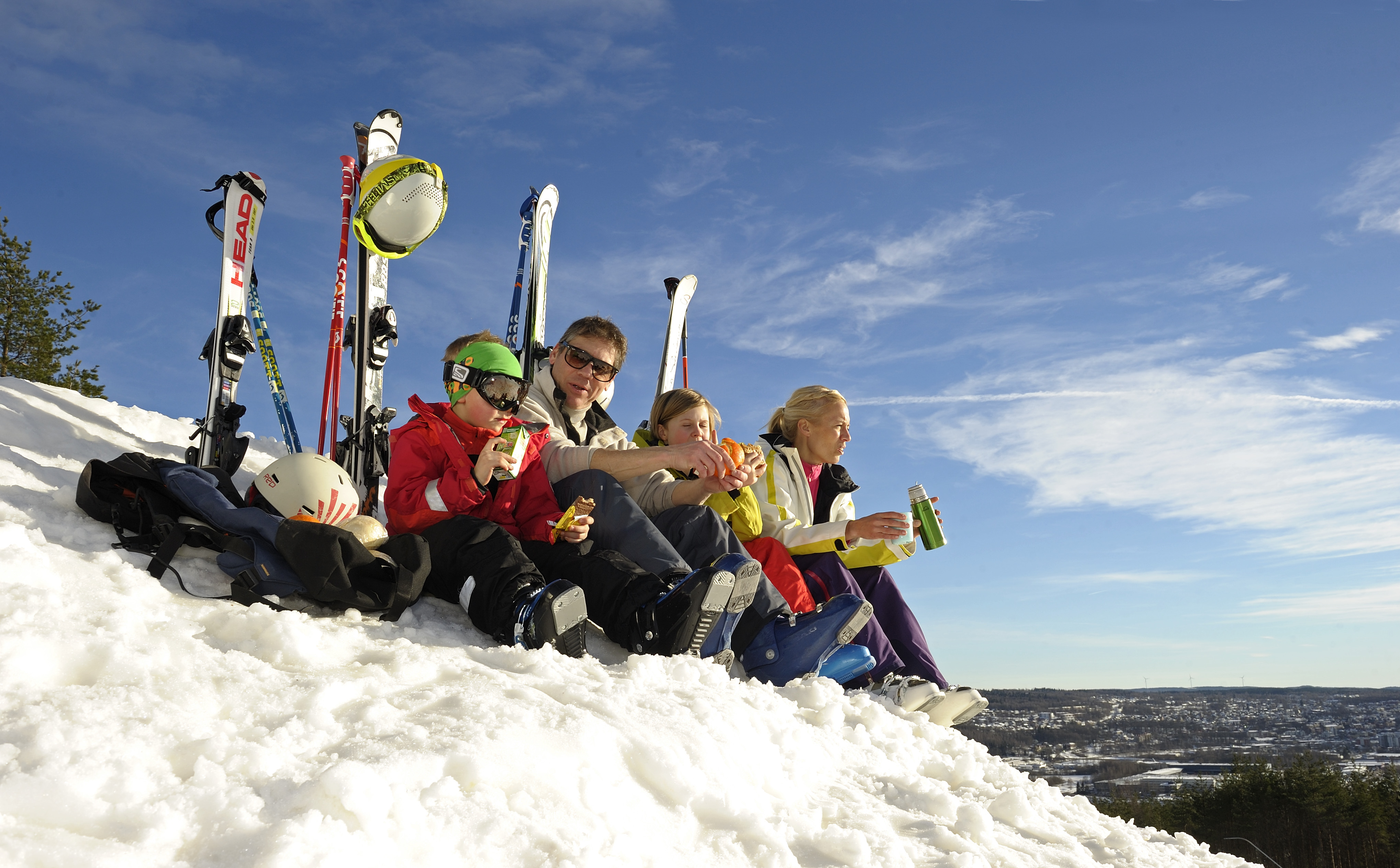Familj sitter i snön med skidor uppställda bakom sig