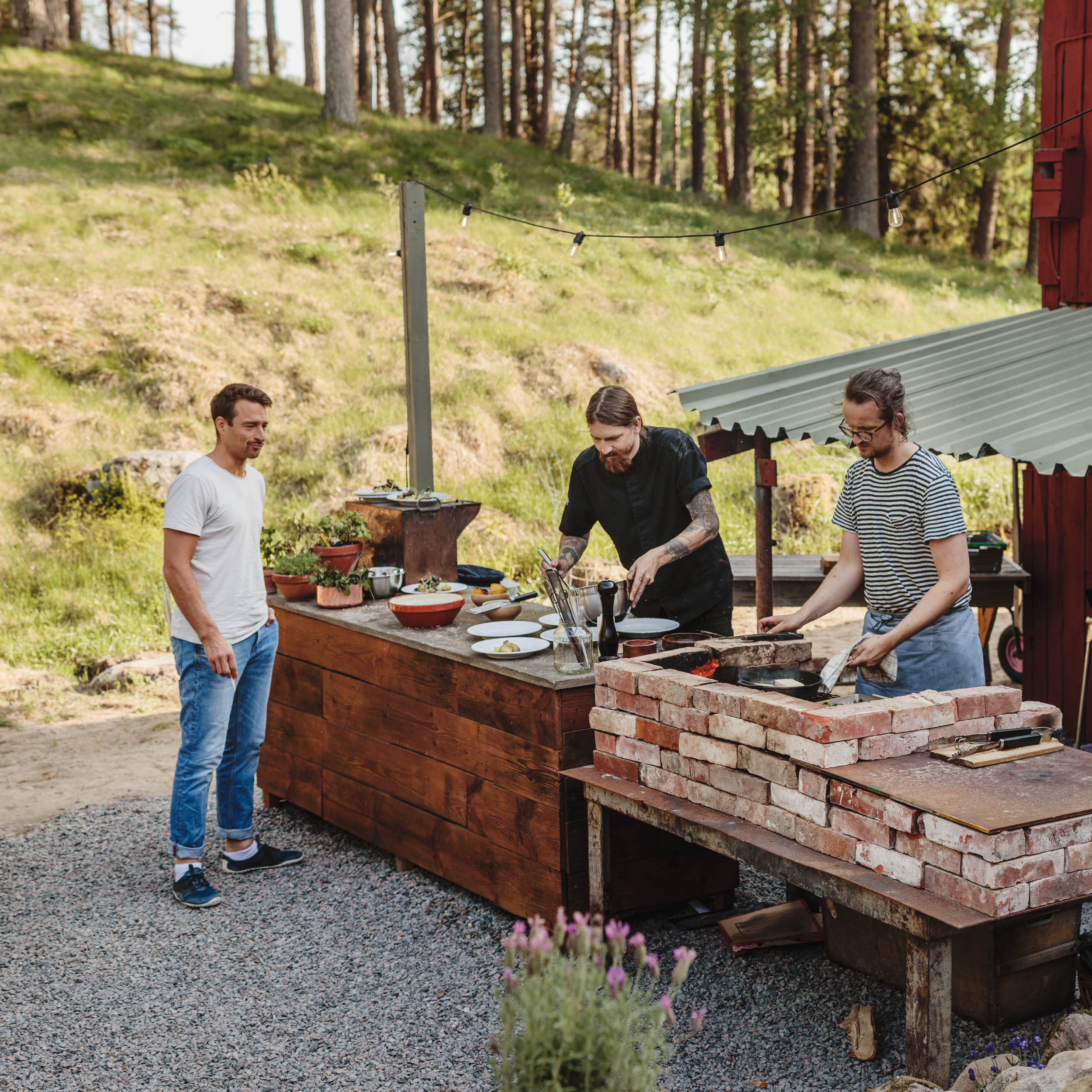 Tre män som står och lagar mat utomhus.