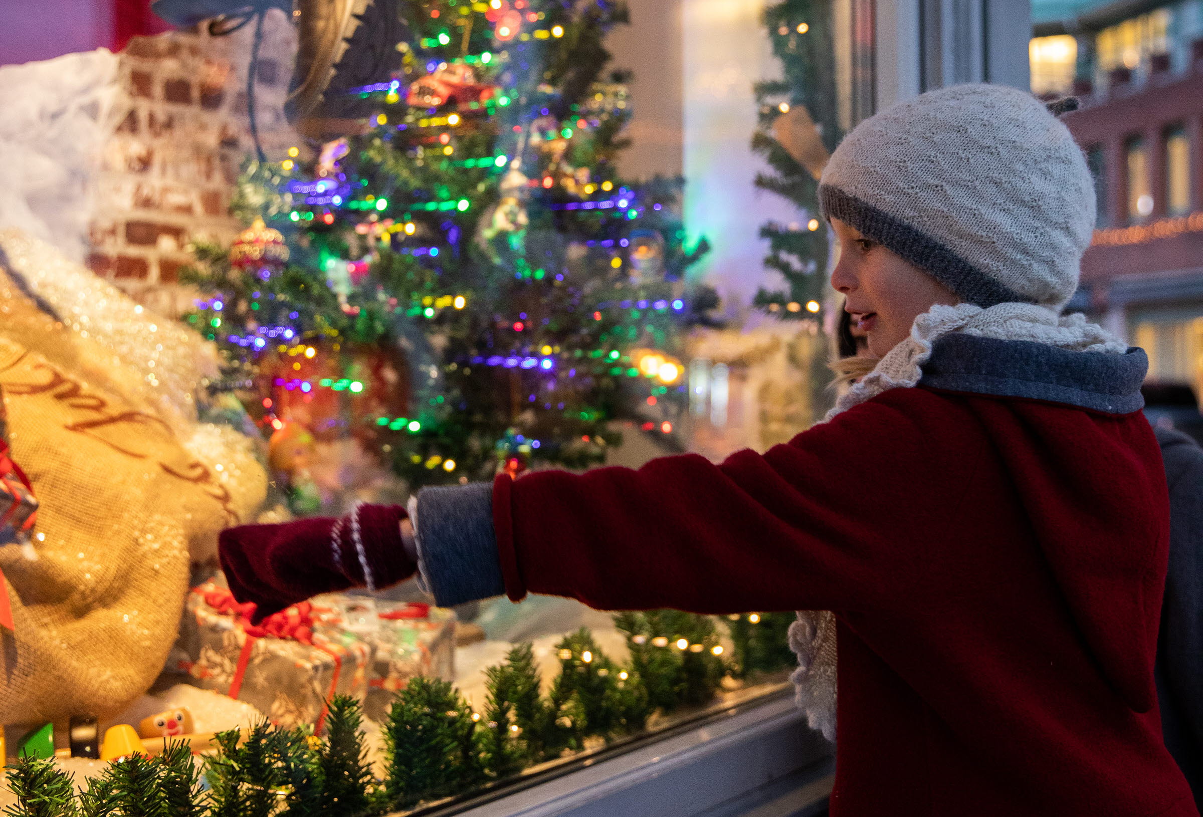 En flicka står och pekar in i ett julskyltat fönster