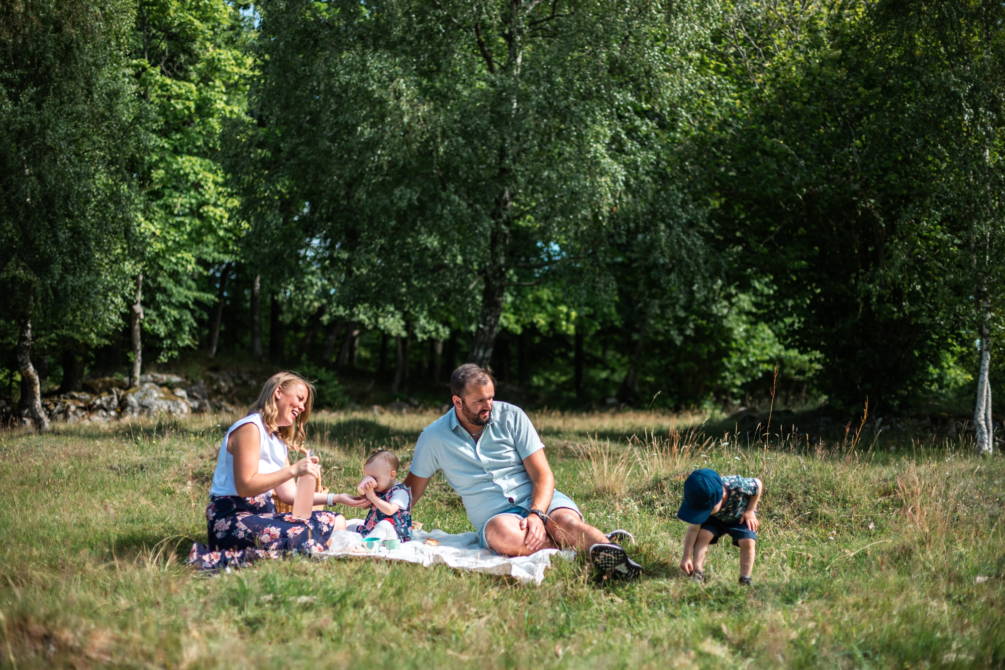 En familj på med två barn sitter och har picknick i det gröna. 