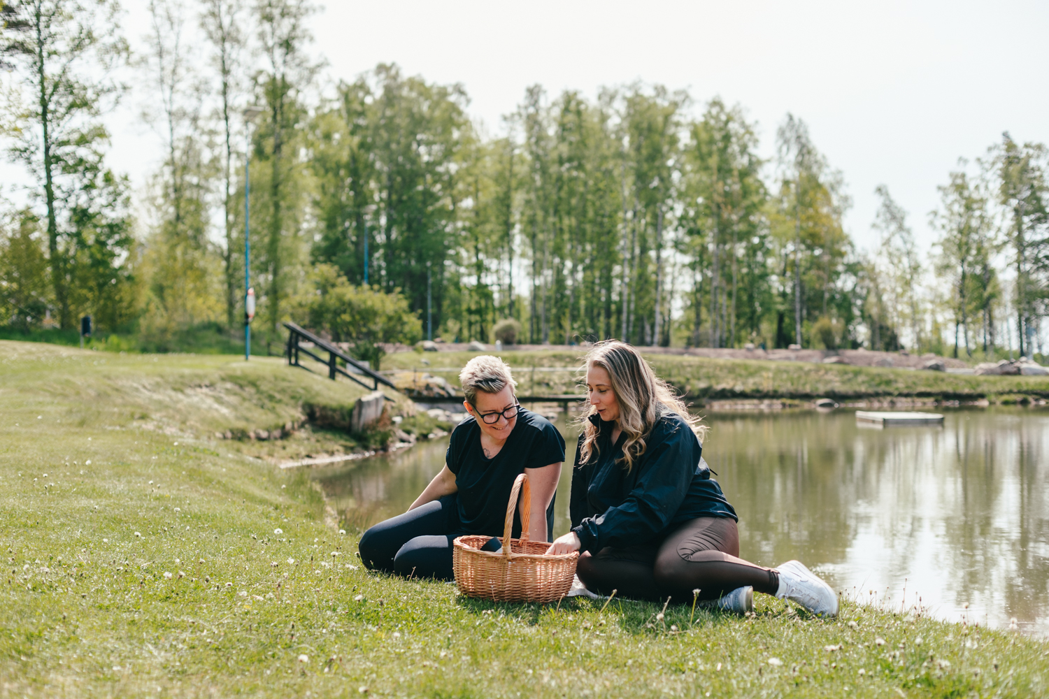 Två kvinnor sitter vid vattnet och har picknick. 