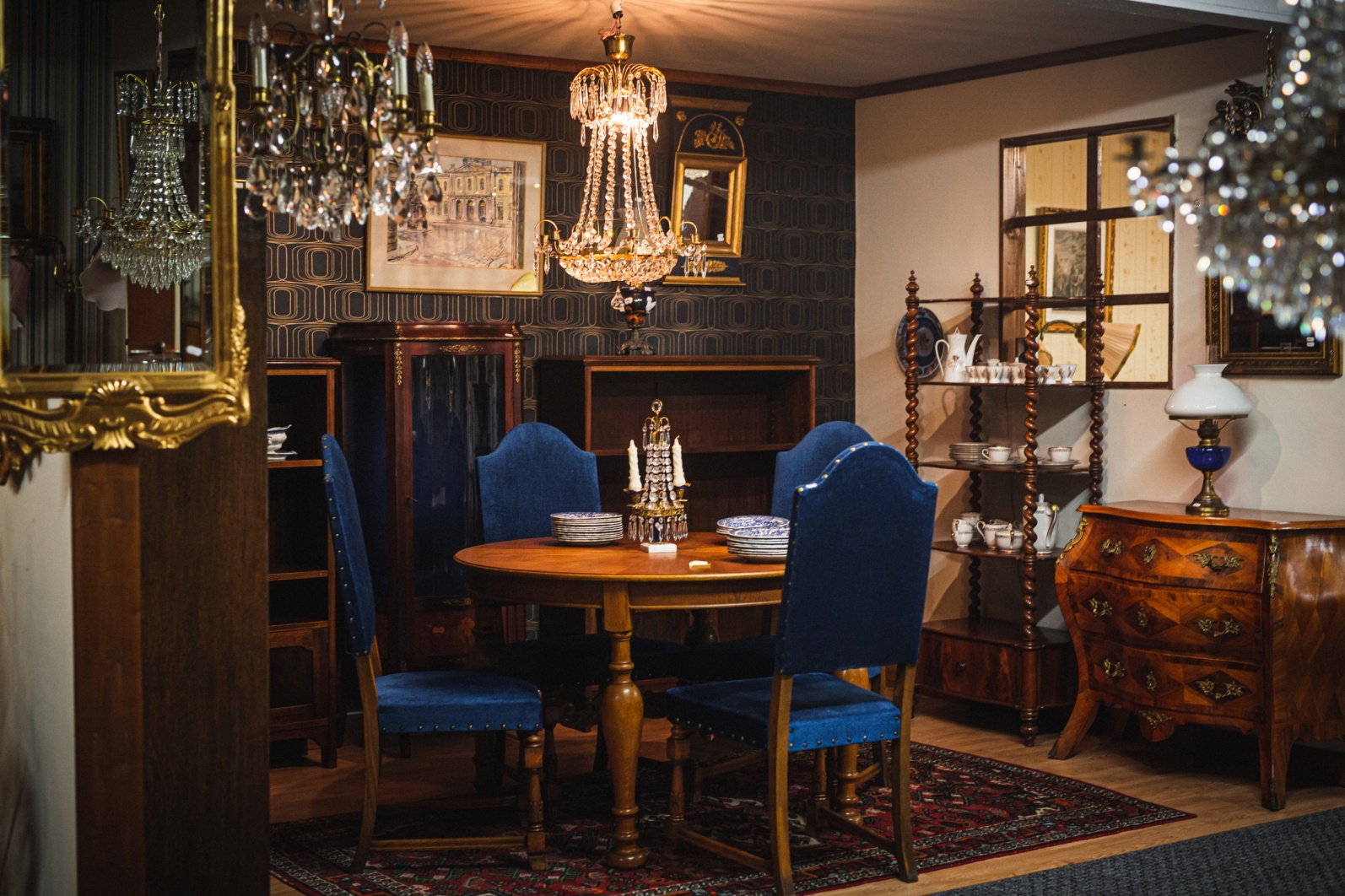Ett möblerat rum med antika möbler. Blå sammet stolar runt ett bord och flera kristallkronor hänger i taket. 