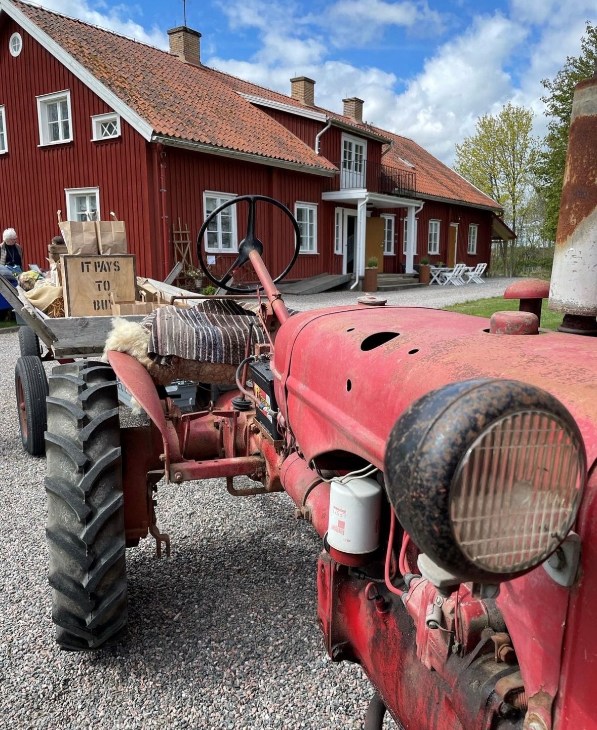 Röd gammal traktor framför ett rött trähus. 
