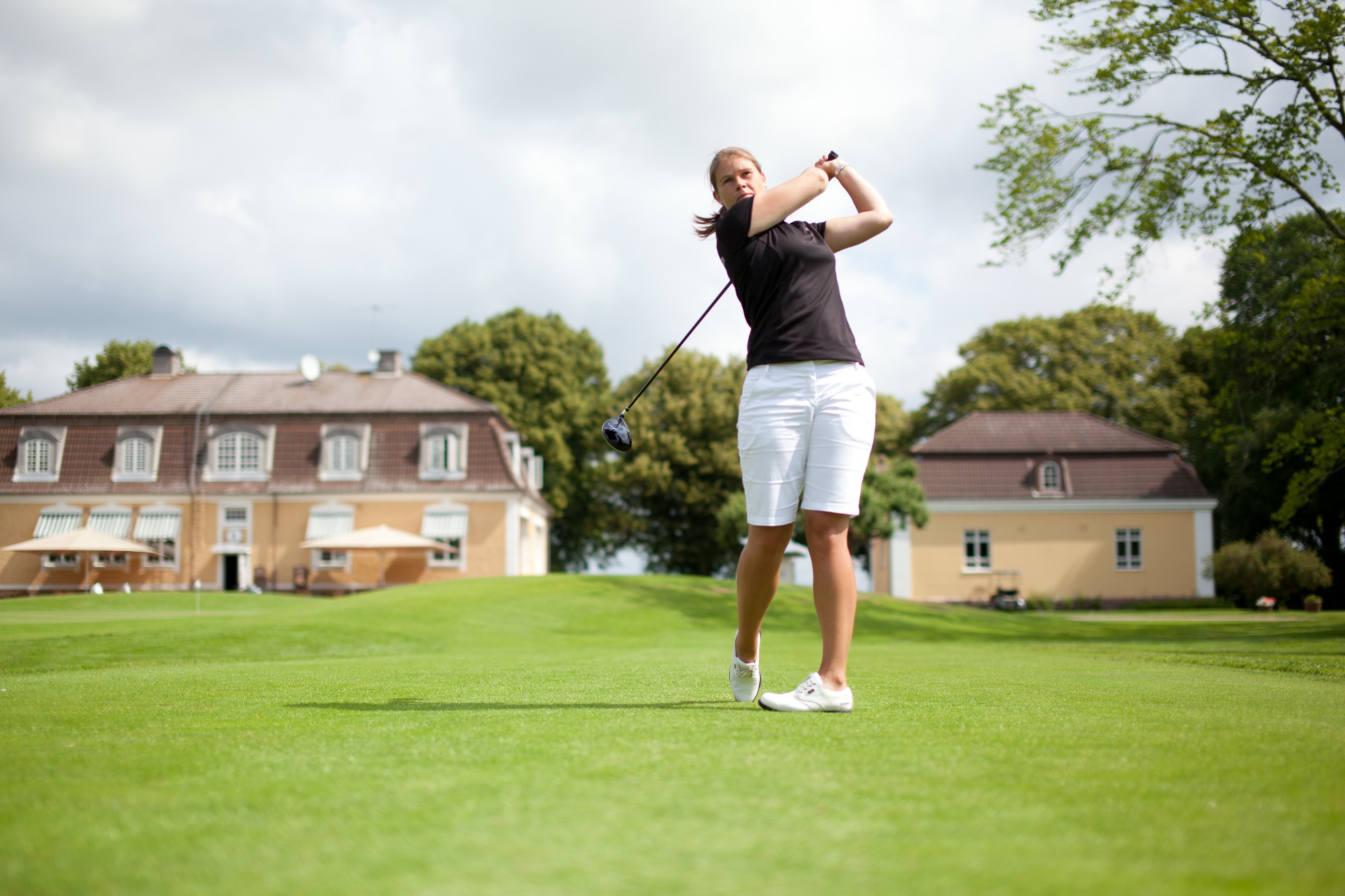 En kvinna står och har precis slagit iväg sin golfboll på golfbanan vid Bjertorp i Vara.