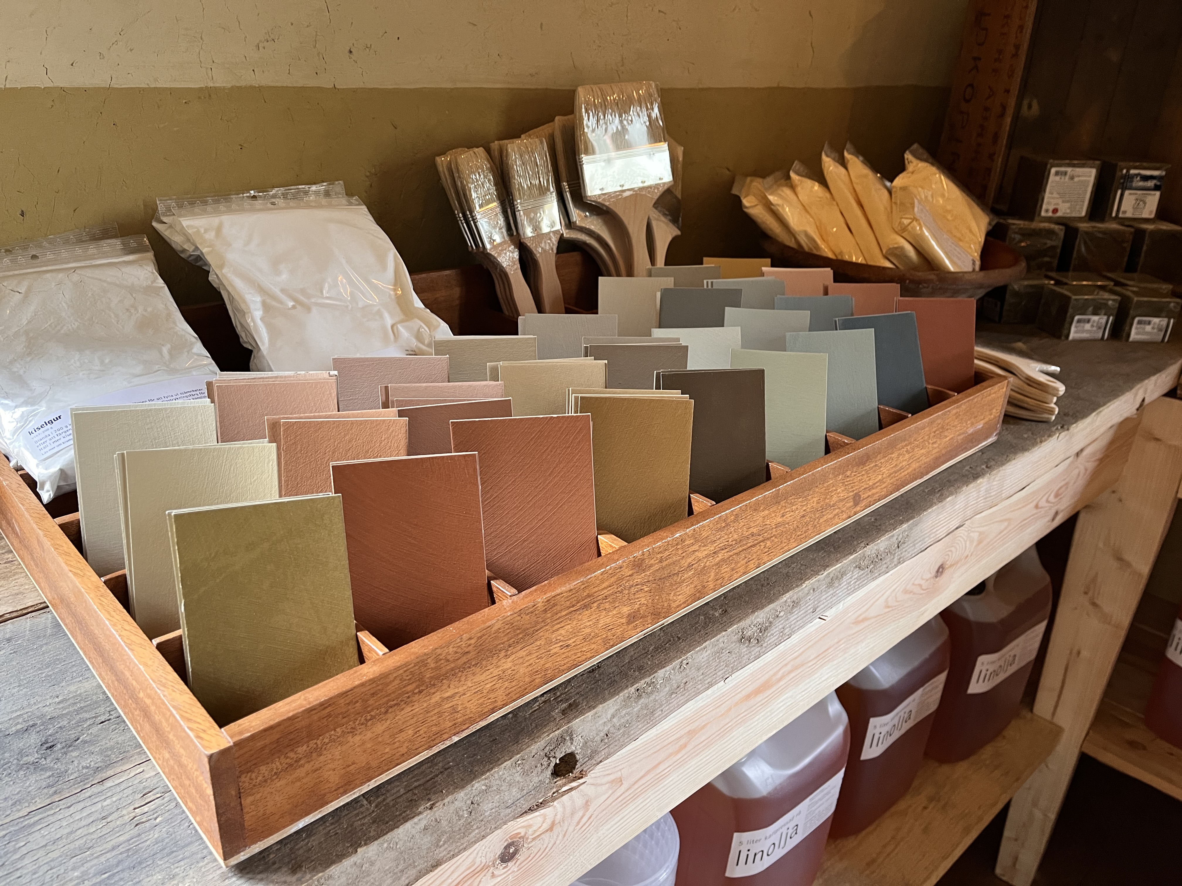 Färgkort i olika färger på ett bord med penslar bakom. 