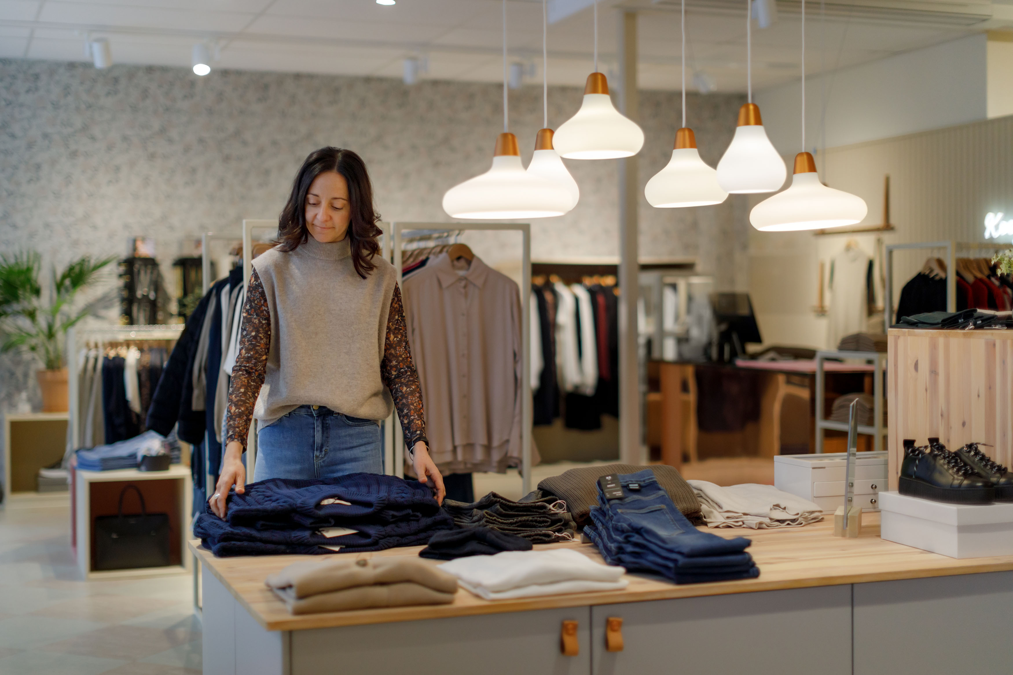 En kvinna står framför ett bord med kläder i en butik.