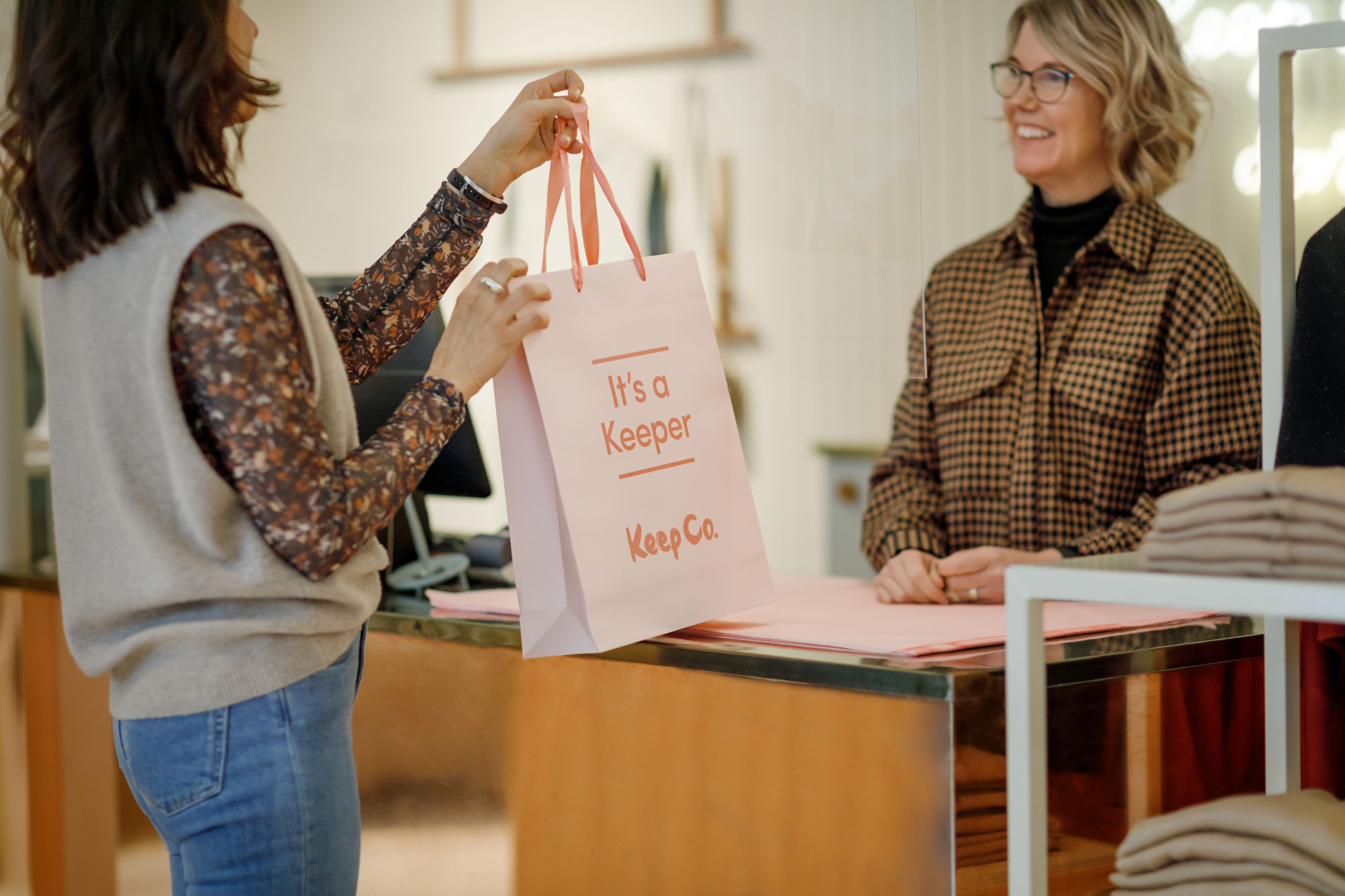 En kvinna står vid en disk. Hon lämnar en kasse med kläder till en kund som står på den andra sidan.