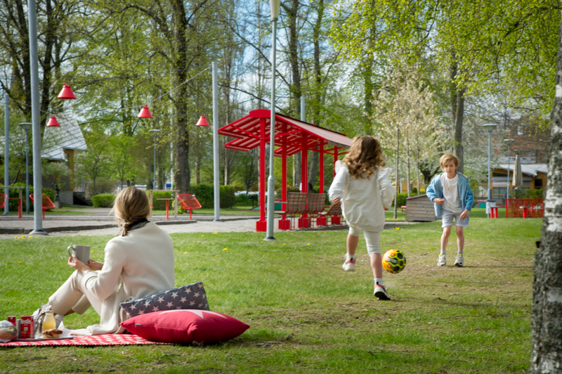 Två barn spelar fotboll i en park och en vuxen tittar på