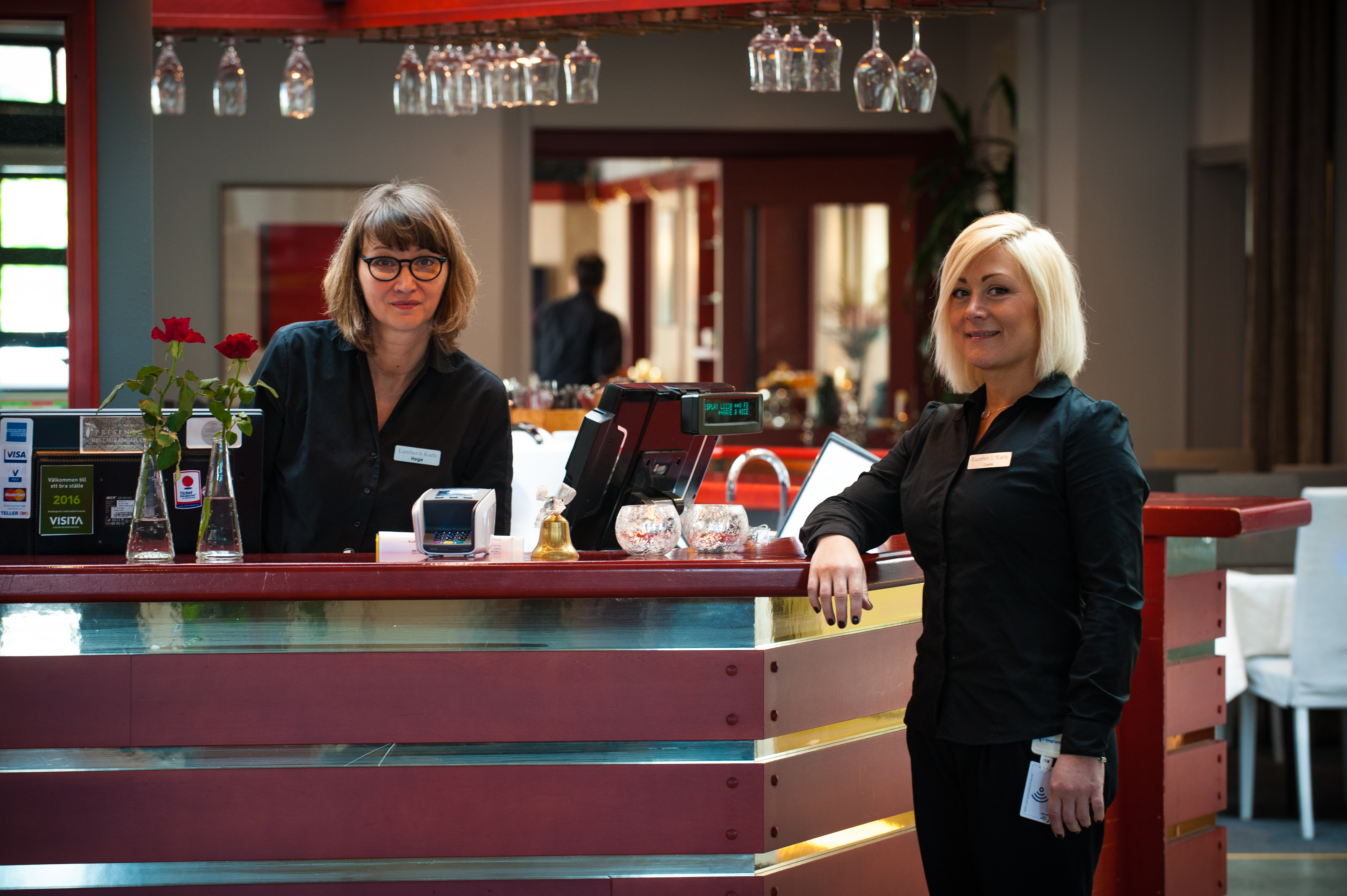 Två kivnnor står vid en hotellreceptionsdisk och ler.