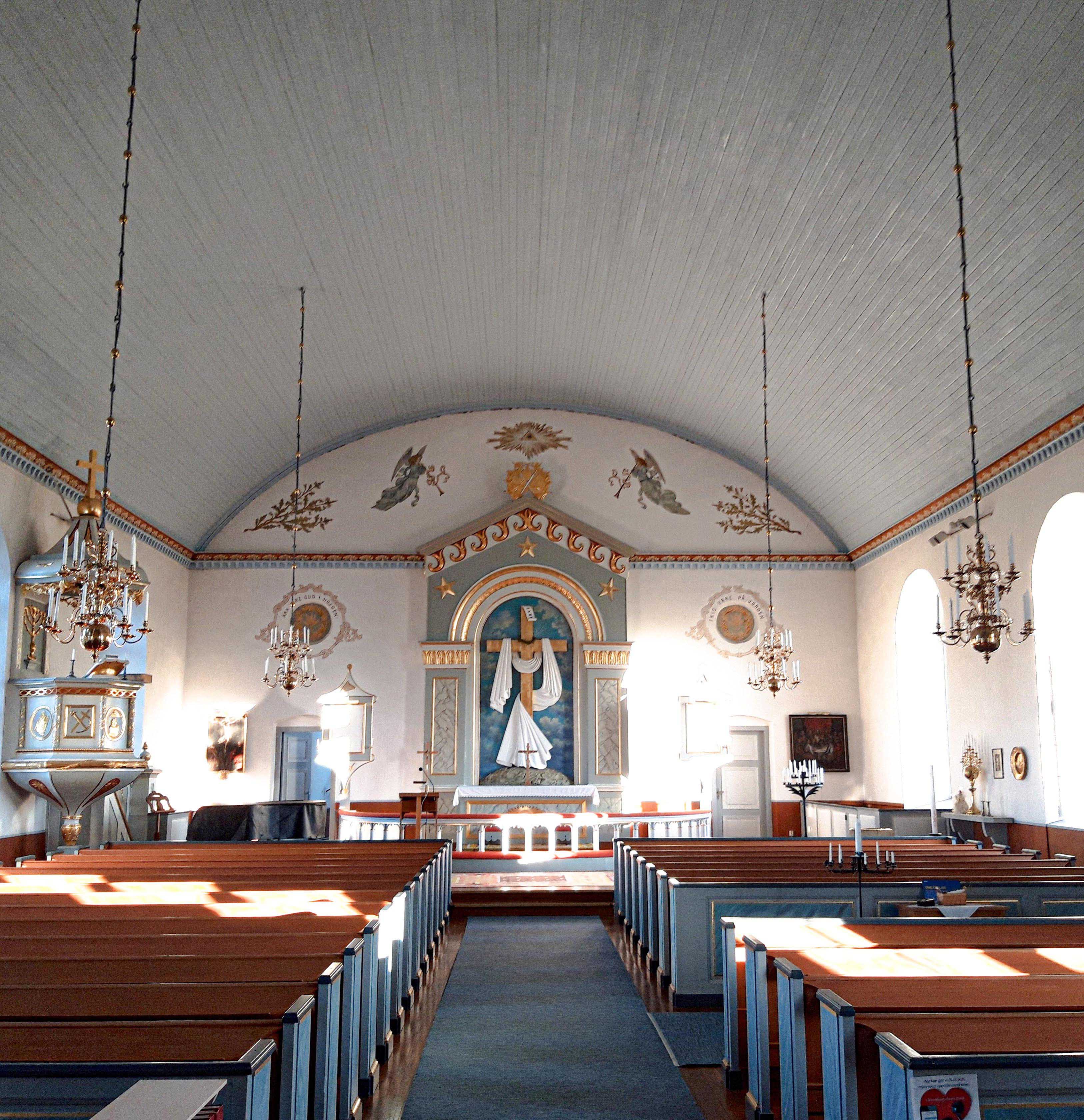 Interiör från en träkyrka med röda och blåa bänkar och en altartavla i blått och vitt längst fram