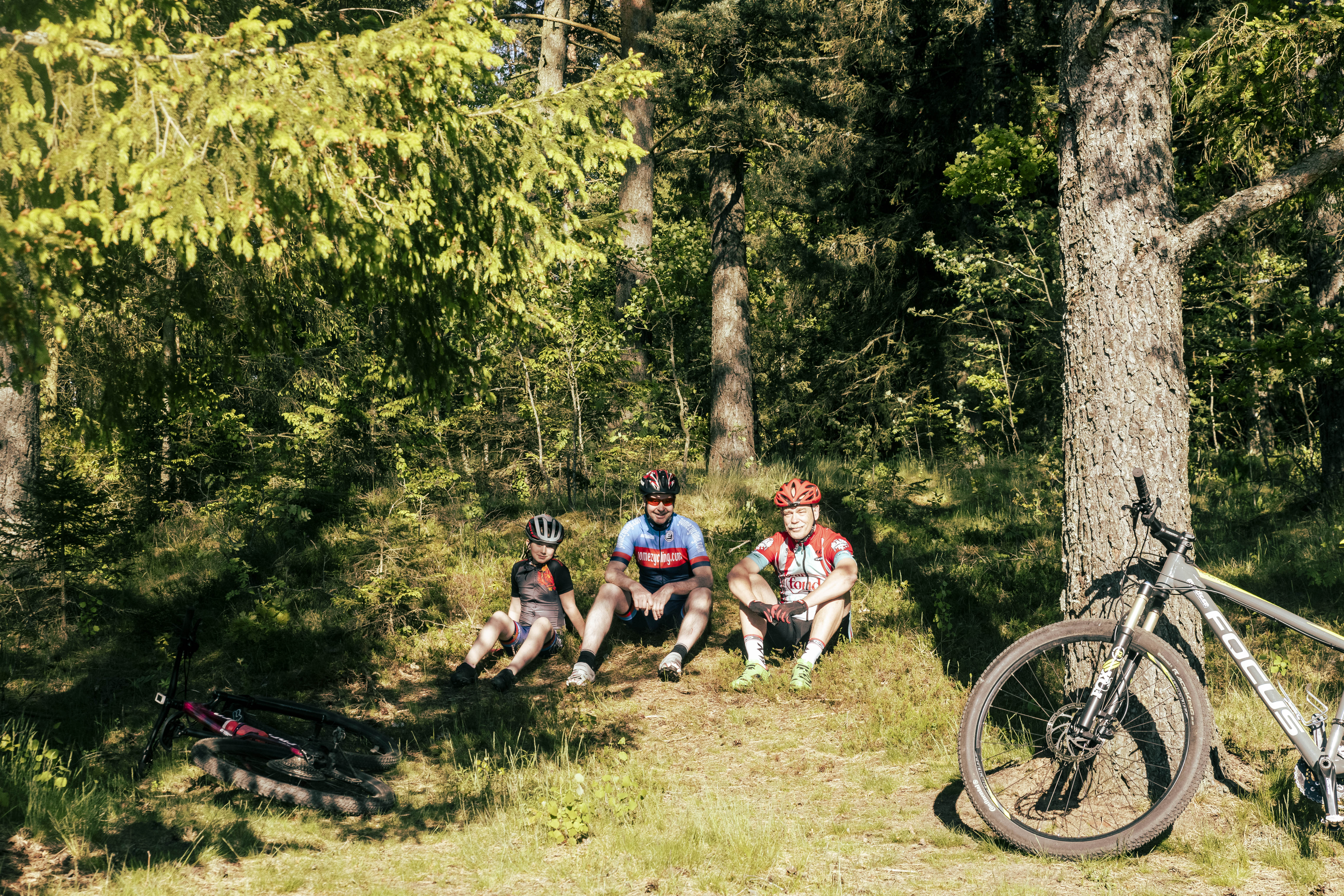 Tre cykelklädda män som sitter i skogskanten.