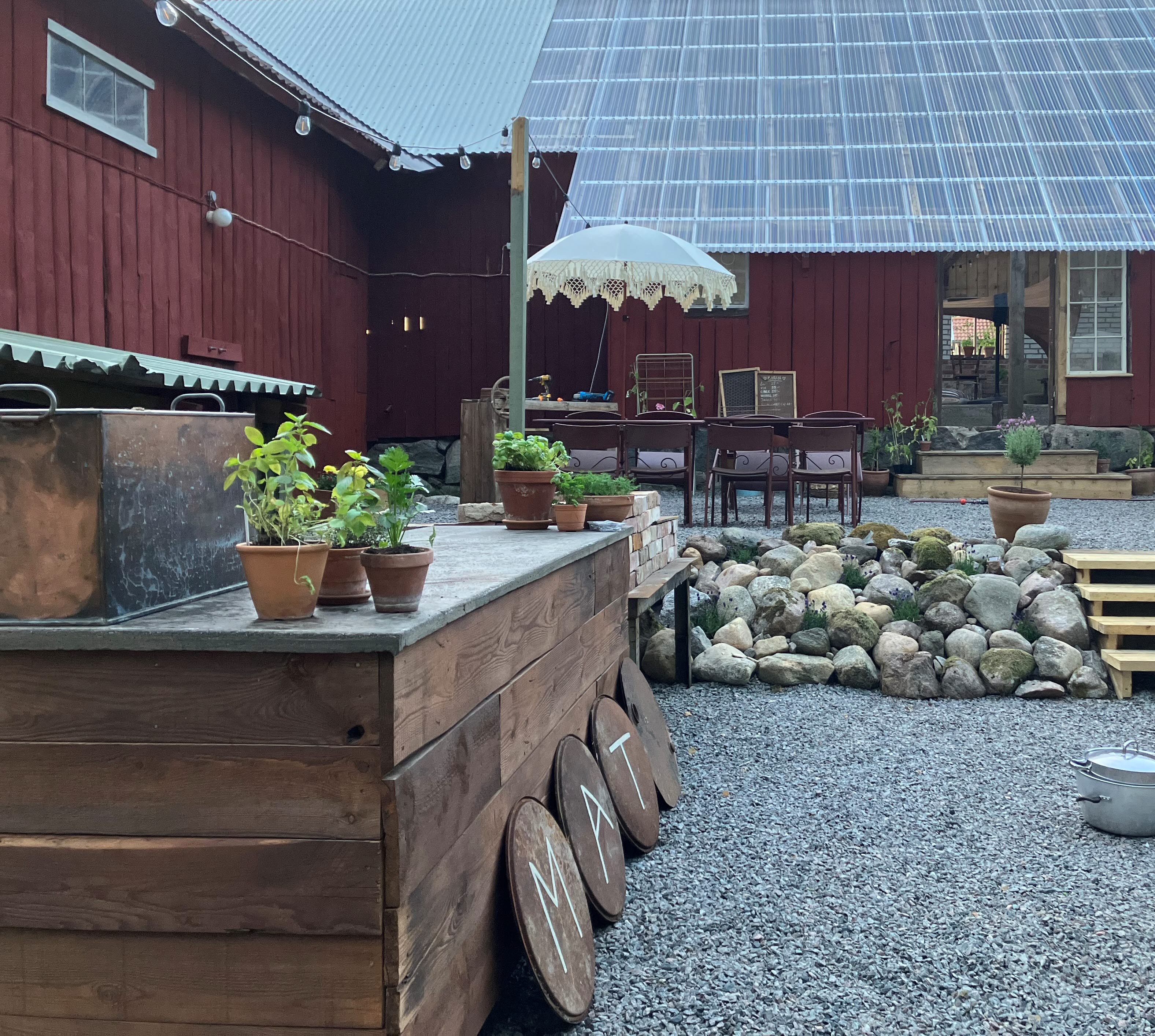 En röd ladugård  med parasoll, en barn och stenar framför. 