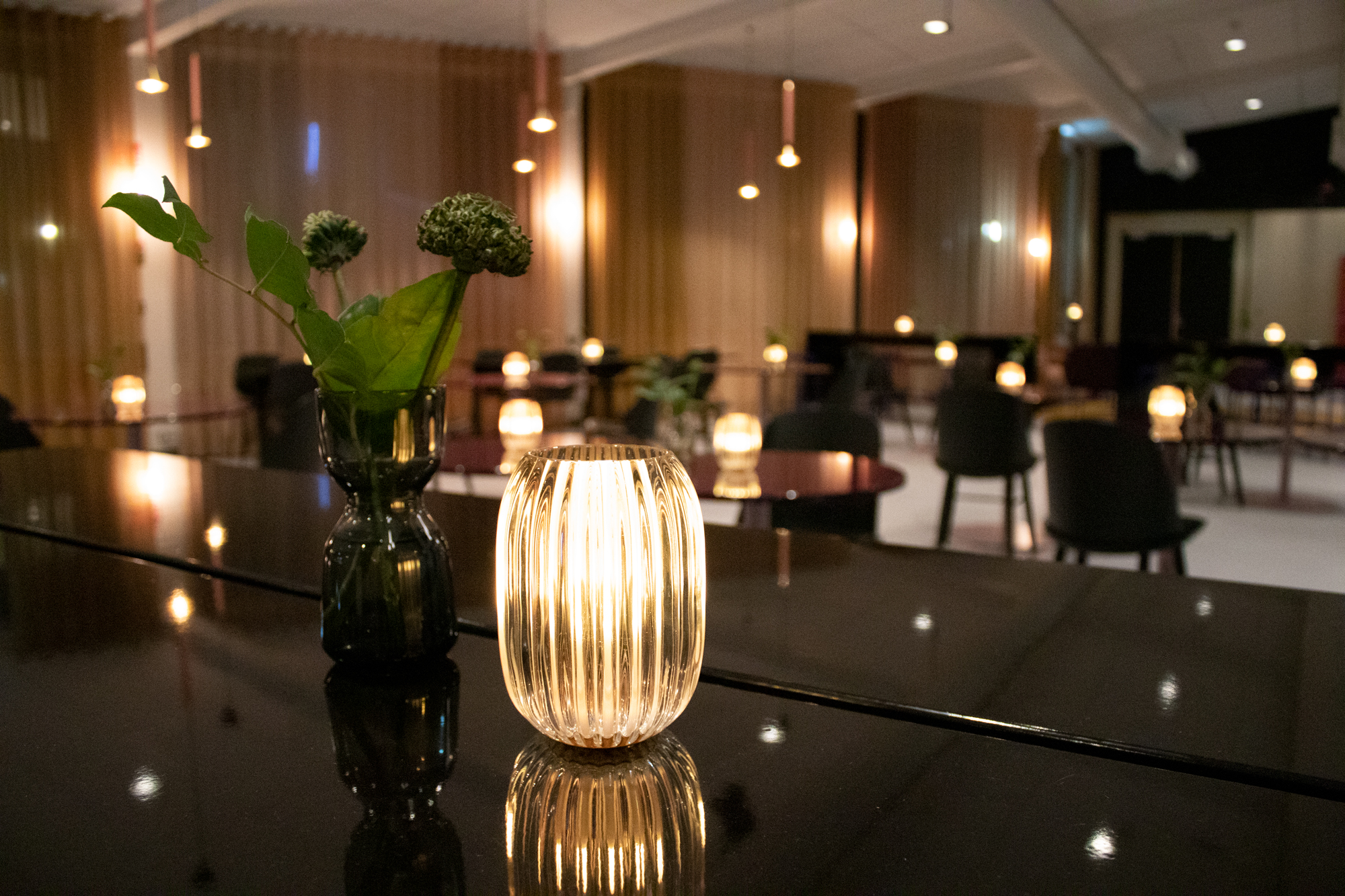 A lamp is standing o a black piano and behind the piano there are black chairs on the floor.