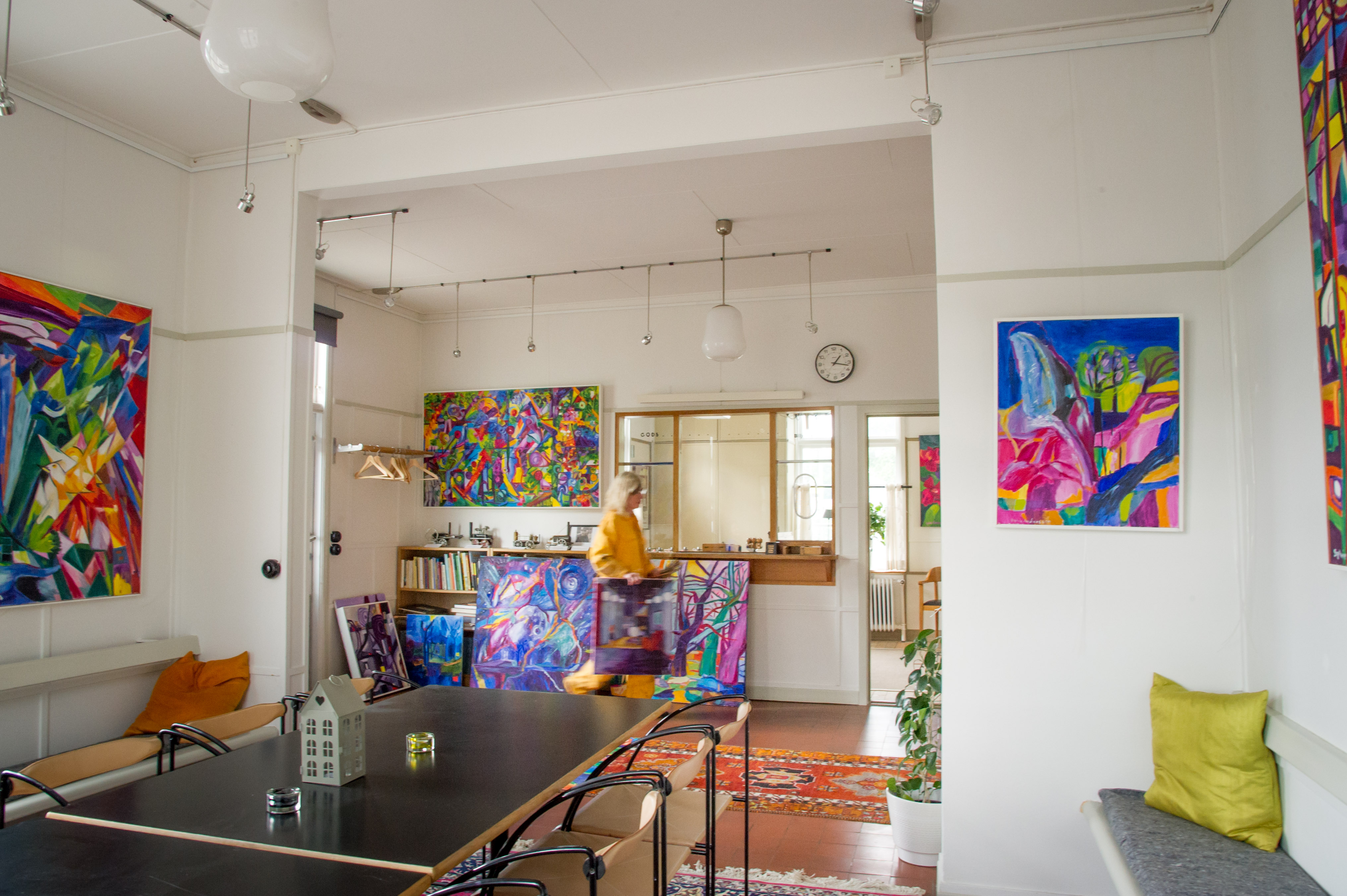 Ett vitt rum med färgglada tavlor på väggarna och ett bord i mitten